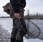 Person holding a Fishpond fishing net by a river with waders on
