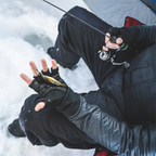 Person in winter clothing sitting on snow, holding fishing gear.