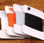 Set of four  Polypropylene Yarn packages in orange, white, gray, and black on a wooden surface