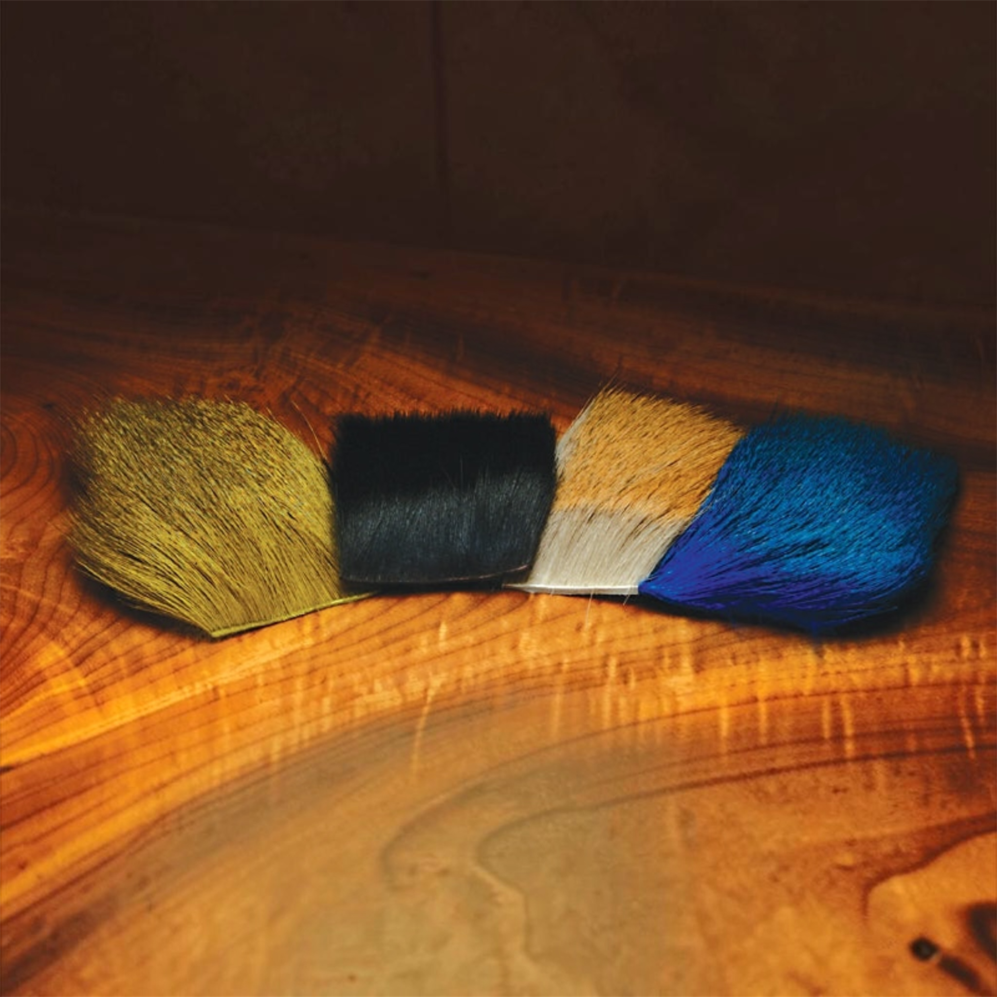 Four swatches of different colored Hareline Dyed Deer Body Hair on a wooden surface