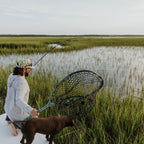 Man with a dog holding a fishing net in a marshy area