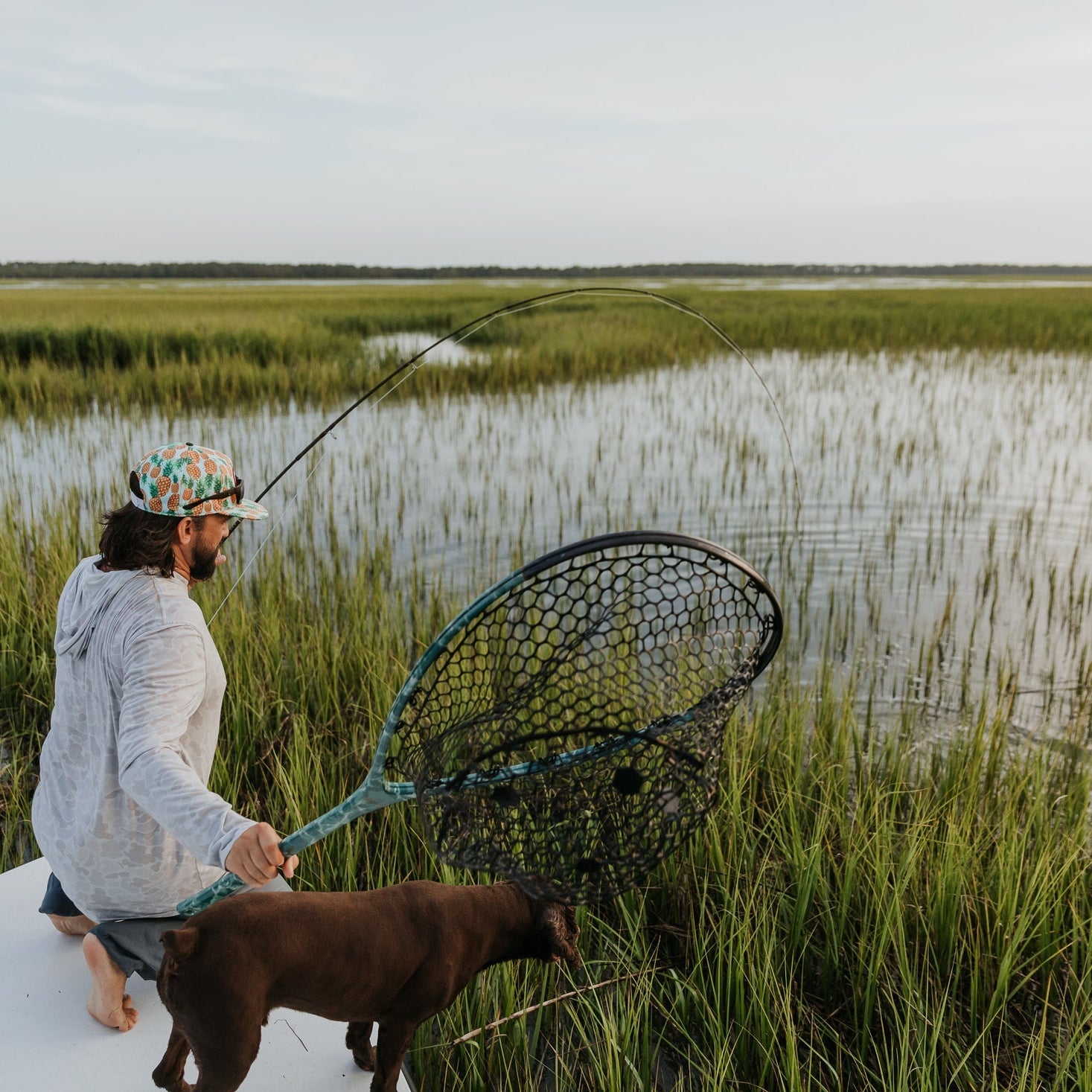 Man with a dog holding a fishing net in a marshy area
