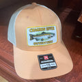 A tan and white trucker hat with a 'Chagrin River Outfitters' fish patch on the front and a 'Richardson 115' size label on the side, photographed on a dark wood floor.