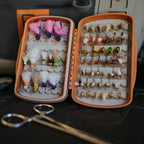 Open orange Fishpond Tacky Pescador small fly box displaying an organized array of fishing flies on a dark surface.