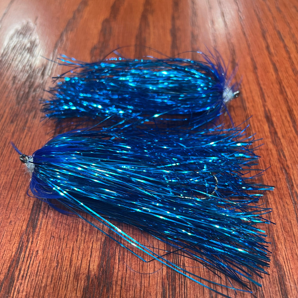 Two artificial fishing flies patterns designed for steelhead fishing, laid out on a wooden surface.
