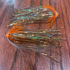 Two artificial fishing streamer patterns designed for steelhead fishing, laid out on a wooden surface.