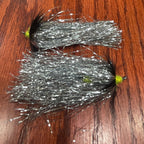Two artificial fishing flies streamers patterns designed for steelhead fishing, laid out on a wooden surface.