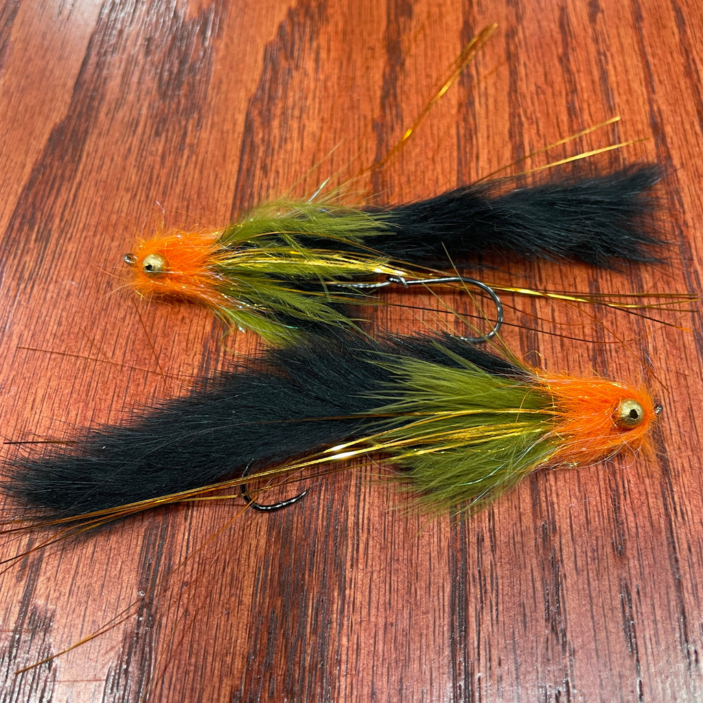 Two black and orange artificial fishing flies designed for steelhead and salmon fishing, laid out on a wooden surface.