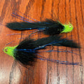 Two black and chartreuse artificial fishing flies designed for steelhead and salmon fishing, laid out on a wooden surface.