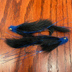 Two black and blue artificial fishing flies designed for steelhead and salmon fishing, laid out on a wooden surface.