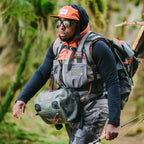 Man in outdoor gear with fishing equipment in a forest setting