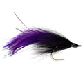 A fishing fly for Tarpon fishing with black and purple feathers on a white surface.