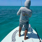 Person fishing on a boat in open water with clear blue skies and a SA Launch Pad at its feet. 