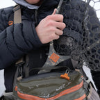 Person holding a Fishpond fishing net with a backpack in a snowy environment