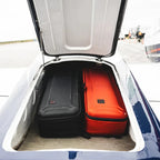 Two Simms Tailwind Rod & Reel Vault suitcases, one black and one red, in the open trunk of a plane.