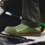 Green rubber Simms MEN's Challenger 7" Deck Boot with brand logo worn by a person on a blurred outdoor background