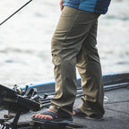 Person fishing on a boat wearing beige Simms MEN's Rogue Softshell Pants and a blue jacket.