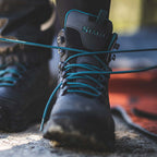 Black Simms WOMEN's Freestone Wading Boot - Rubber Soles with teal laces on a blurred natural background
