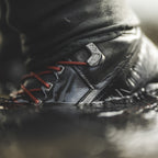 Close-up of a black Simms MEN's G3 Guide Wading Boot - Felt Soles with red laces on a blurred background