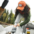 Person tying a Simms MEN's Pursuit Shoe Riffle on a boat with a forest background