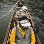 Two people in a canoe on a river with a forested shoreline.