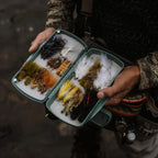 Person holding a Fishpond Tacky Pescador Fly Box - Large - Dynamic Foam of fly fishing flies on a dark background