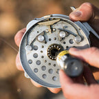 Close-up of a person repairing a fishing reel with a blurred natural background