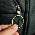 Hand holding a yellow keychain with a metal clip against a black bag.