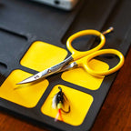 Yellow scissors on a black and yellow foam block with a fishing lure.