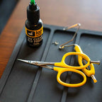 Yellow Loon Ergo Tungsten Carbide Curved Micro Tip Scissors w/ Precision Peg and a bottle of UV clear finish on a dark surface