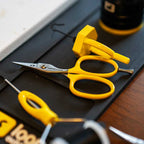 Yellow-handled Loon Ergo Tungsten Carbide Universal Scissors w/ Precision Peg on a dark surface with blurred background