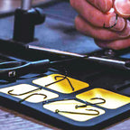 Fishing hooks on a holder with a hand selecting one, blurred background