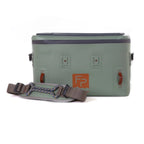 A green Fishpond Cutbank Gear Bag with orange trim and a visible orange logo on the front, equipped with a strap and a handle.