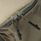 Close-up of a beige fabric with a zipper and drawstring, showing water droplets.