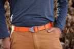 Person wearing a blue shirt, brown pants, and an orange belt with a silver buckle.