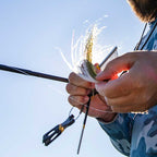 Person preparing a fishing rod with a blue sky background