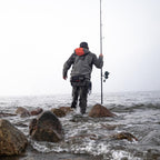 Person fishing from rocks in a body of water on a cloudy day wearing a Simms MEN's G3 Guide Jacket