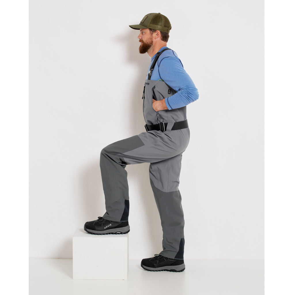 A fisherman with a pair of gray zippered Orvis men's PRO fly-fishing waders with suspenders and boots.