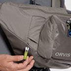 A gray Orvis sling pack designed for fly-fishing, featuring multiple storage compartments and oa water bottle holder.