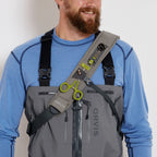 A man wearing a gray Orvis sling pack designed for fly-fishing, featuring multiple storage compartments and oa water bottle holder.