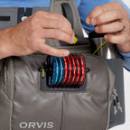 A gray Orvis sling pack designed for fly-fishing, featuring multiple storage compartments and oa water bottle holder.