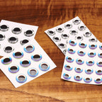 Two sheets of Hareline 3D Big Fish Eyes Adhesive Holographic Eyes on a wooden surface