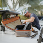A gray and brown Fishpond fishing rod and reel case with a strap and orange trim laying on a boat deck.