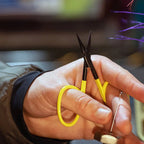 Person holding a pair of scissors with yellow handles cutting a purple string.