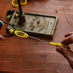 Person holding a yellow Loon Ergo Bobbin Threader on a wooden surface with tools in the background