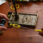 Person using a yellow Loon Ergo Bobbin Threader with a wooden surface and tools in the background