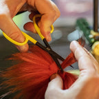 Person cutting red hair with yellow-handled scissors in a blurred indoor setting