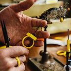 Close-up of hands holding a yellow Loon Gator Grip Dubbing Spinner with a blurred workshop background