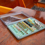 Clear fly fishing box with green interior  and flies on a wooden surface