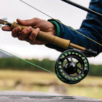 Fishing rod with Sage Spectrum Fly Reel held by a person, blurred natural background